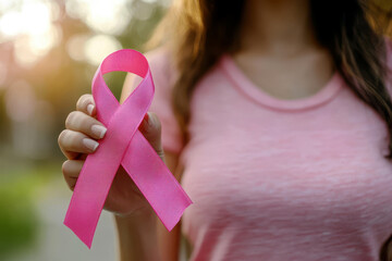 Woman hand holding a pink ribbon for breast cancer awareness on blur background. - Powered by Adobe