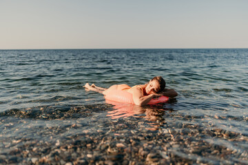A woman is floating on a pink inflatable raft in the ocean. The water is calm and the sky is clear. The woman is enjoying her time in the water.
