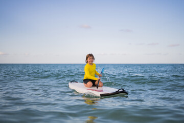 Kid riding on a paddle board. Summer holidays. Kid paddle surf surfer little blonde boy in summer beach. Happy Child floating on a paddleboard in the ocean. Kid doing paddle in summer.