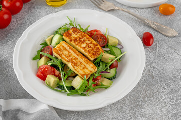 Salad with grilled halloumi cheese, tomatoes, avocado, cucumber and olive oil on a concrete background. Healthy food. Top view