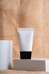 Plastic white tube for cream or lotion. Skin care or sunscreen cosmetic with stylish props on wood background.