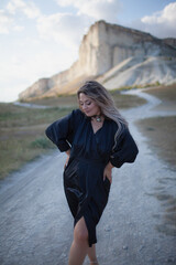 A woman plus size dressed in a dress walking against the background of a white mountain. Beautiful girl with a long hair developing in the wind travels