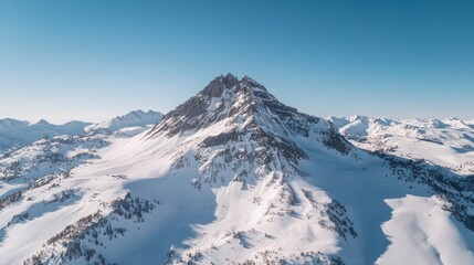 Aerial view of a snowy mountain peak under a clear blue sky.
