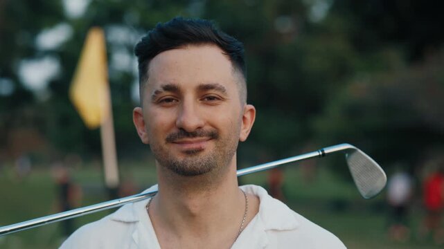Confident golf player with three day stubble turning head to camera in park portrait. close up portrait of handsome golfer holds steel club on shoulder outdoors. Guy takes part in competition