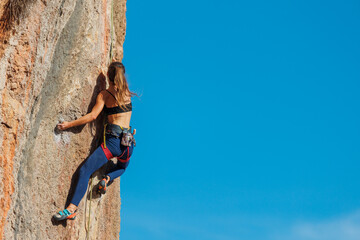 The girl climbs the rock. The climber is training to climb the rock. A strong athlete overcomes a...