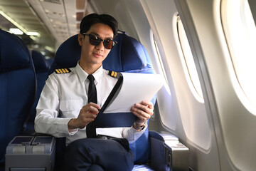 Asian pilot sitting in an airplane seat with clipboard hands reviewing or completing some paperwork