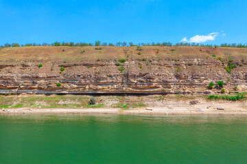 Rocky shoreline with a body of water in the foreground. River beside a towering cliff, creating a serene coastal scene