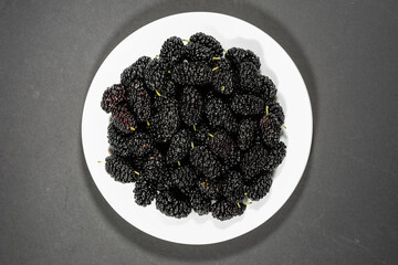 Fresh black mulberry on white plate on dark background. Concept of juicy and healthy seasonal...