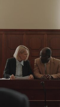 Vertical over the shoulder shot of Caucasian female prosecutor and African American male plaintiff discussing case points at court hearing