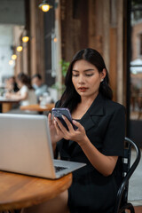 An attractive Asian businesswoman is using her smartphone while working remotely from a cafe.