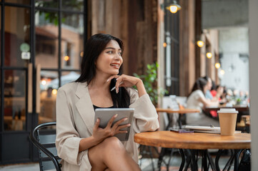 A positive, gorgeous Asian businesswoman is looking away, holding a digital tablet, and daydreaming.
