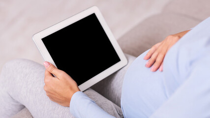 Pregnancy App. Unrecognizable Expectant Lady Using Digital Tablet With Empty Screen Sitting On Couch Indoor. Mockup, Cropped