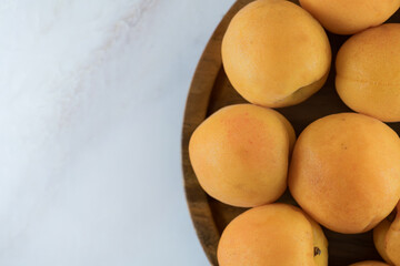 Ripe apricots on a wooden plate, top view. Fresh natural apricots, delicious summer dessert, on marble countertop, close-up, high resolution.