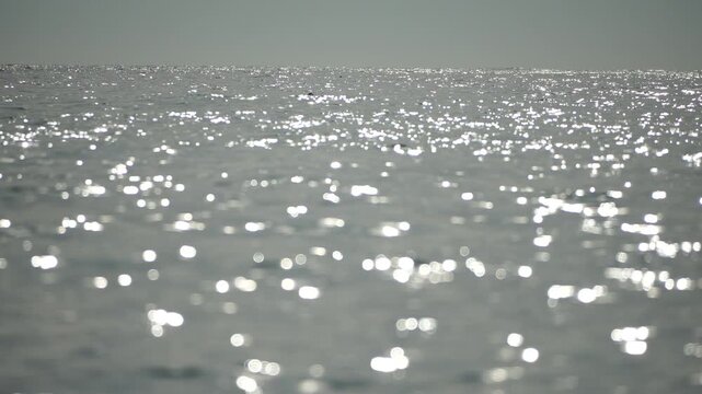 Blurred golden sea at sunset with shifting focus and bokeh effect. Sun reflects and sparkles on waves, illuminating golden sea. Holiday recreation concept. Abstract nautical summer ocean sunset nature
