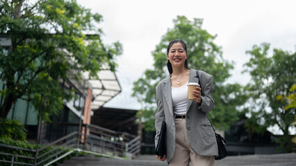 An attractive Asian businesswoman is smiling at the camera and walking in the city.