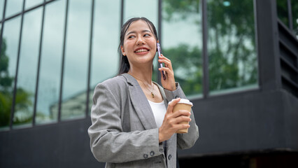 Confident, beautiful Asian businesswoman in a suit is talking on the phone while walking in the city