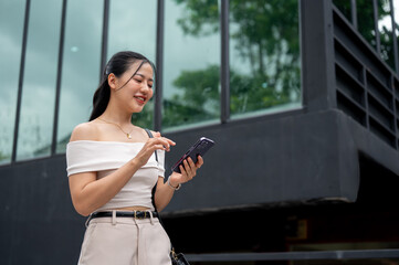 Attractive Asian woman in a trendy outfit is replying chat on her phone while walking in the city.