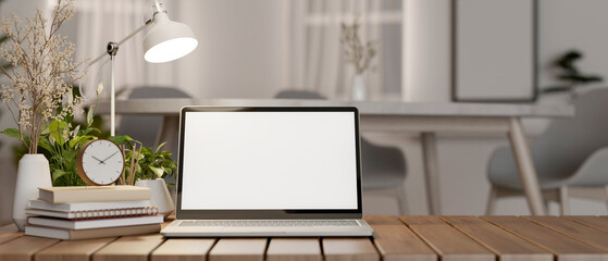 A laptop computer with a white-screen mockup and decor on a wooden table in a minimalist room.