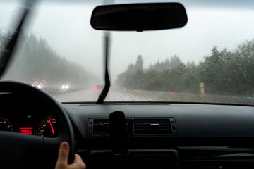 Obraz premium A car is driving along the road during the rain and the windshield wipers are wiping the windshield of the car.