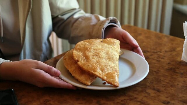 A man's hands are holding a plate of deep-fried patties. Delicious and appetising chebureks on a plate.