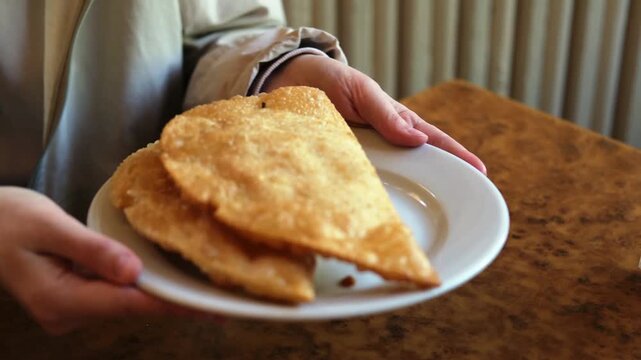 A man's hands are holding a plate of deep-fried patties. Delicious and appetising chebureks on a plate.