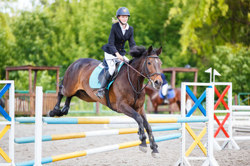 Young horse rider girl clearing an obstacle during her showjumping course at an equestrian...
