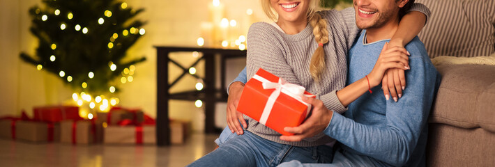 Presents time. Man giving new year present to wife, sitting on floor and enjoying holidays together