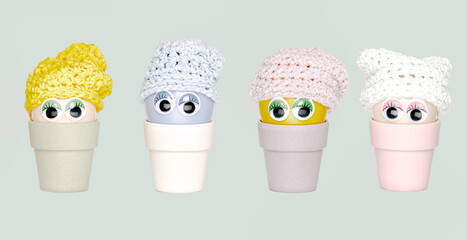 Four plastic eggs with wobbly eyes and knitted hats in bamboo egg holders. Fun for kids.