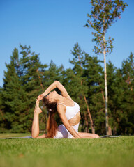 Calm and quiet morning. Young, beautiful woman in activewear doing stretching, yoga exercises at park. Concept of mental and physical health, recreation, balance, nature.