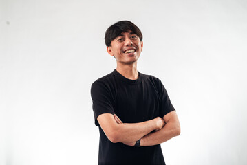 Fototapeta premium A smiling Asian man in a black t-shirt stands confidently with arms crossed against a plain white background, ideal for professional headshots, personal branding, or business profile content