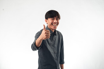 A smiling Asian man in a dark grey button-up shirt gives a thumbs-up gesture while standing against a plain white background, perfect for professional headshots, personal branding, or motivational