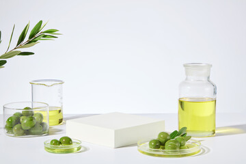 The promotional photo of natural olive extract cosmetic, blank podium in the center for product displaying, surrounded with glassware contain fresh olive and yellow olive oil. Front angle, copy space