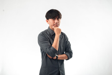 An Asian man in a gray shirt with a thoughtful expression, hand on chin, and one arm crossed,...