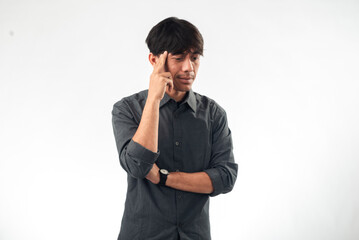 An Asian man in a gray shirt with a thoughtful expression, pointing to his temple with one hand, while the other arm is crossed, standing against a plain white background, as if indicating an idea