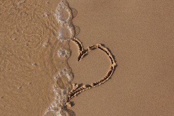 Traces on clean sea sand, a footprint and a drawn heart.