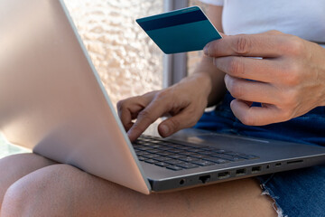 Close-up of woman holding credit card while browsing on laptop.