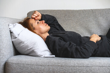 Tired and depressed woman lying down on the sofa. Mental problems, anxiety, overworking.