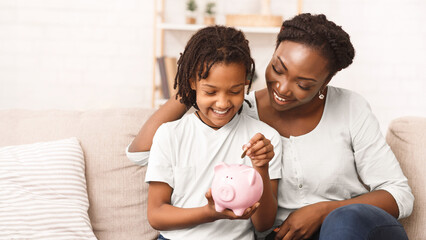 Fototapeta premium Children And Economy. Little African American Girl Putting Coin In Piggybank, Saving Money.