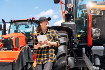 Woman representative at a dealership for construction and agricultural machinery stands next to a...