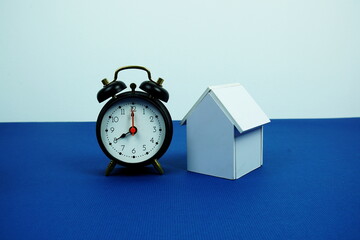 White house model and alarm clock on navy blue background, Mortgage and properties concept