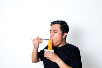 Fototapeta premium Asian adult man wearing a black t-shirt posing eating Korean specialty food odeng isolated white background