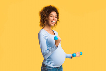 Healthy motherhood. Black pregnant woman exercising with dumbbells over white studio background