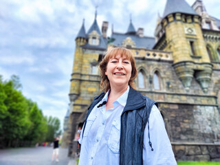 Fototapeta premium A woman enjoys her travel adventure at Garibaldi Castle, showcasing her excitement in a historic setting. The adventures of a middle-aged female tourist on a trip