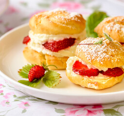 Cream puffs cakes or profiterole filled with whipped cream and served with strawberries and tea on...