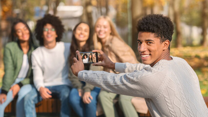 Selective focus on smiling african guy taking photo of his international teen friends, having fun at park