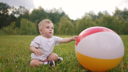 Happy family. baby and toddler playing with a ball in a park. Play child family concept. A baby is sitting on the grass and playing. A toddler is sitting on the grass lifestyle playing with a ball.