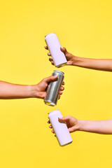 Minimalist mockup with human hands holding aluminum cans against yellow background creating...