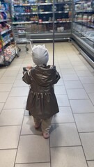 Fototapeta premium child walks through the supermarket. happy family kid dream concept. child shopping in a store. a little girl in a white hat and coat walks and looks at products in a magazine lifestyle