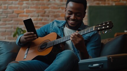 Obraz premium A young man with an acoustic guitar sitting on the couch, smiling and playing.