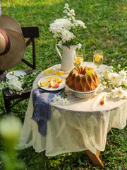 Chamomile flowers, books, glass teapot and cup with herbal tea on table in garden, natural background. summer season. relax time. useful calming tea. tea party outdoor